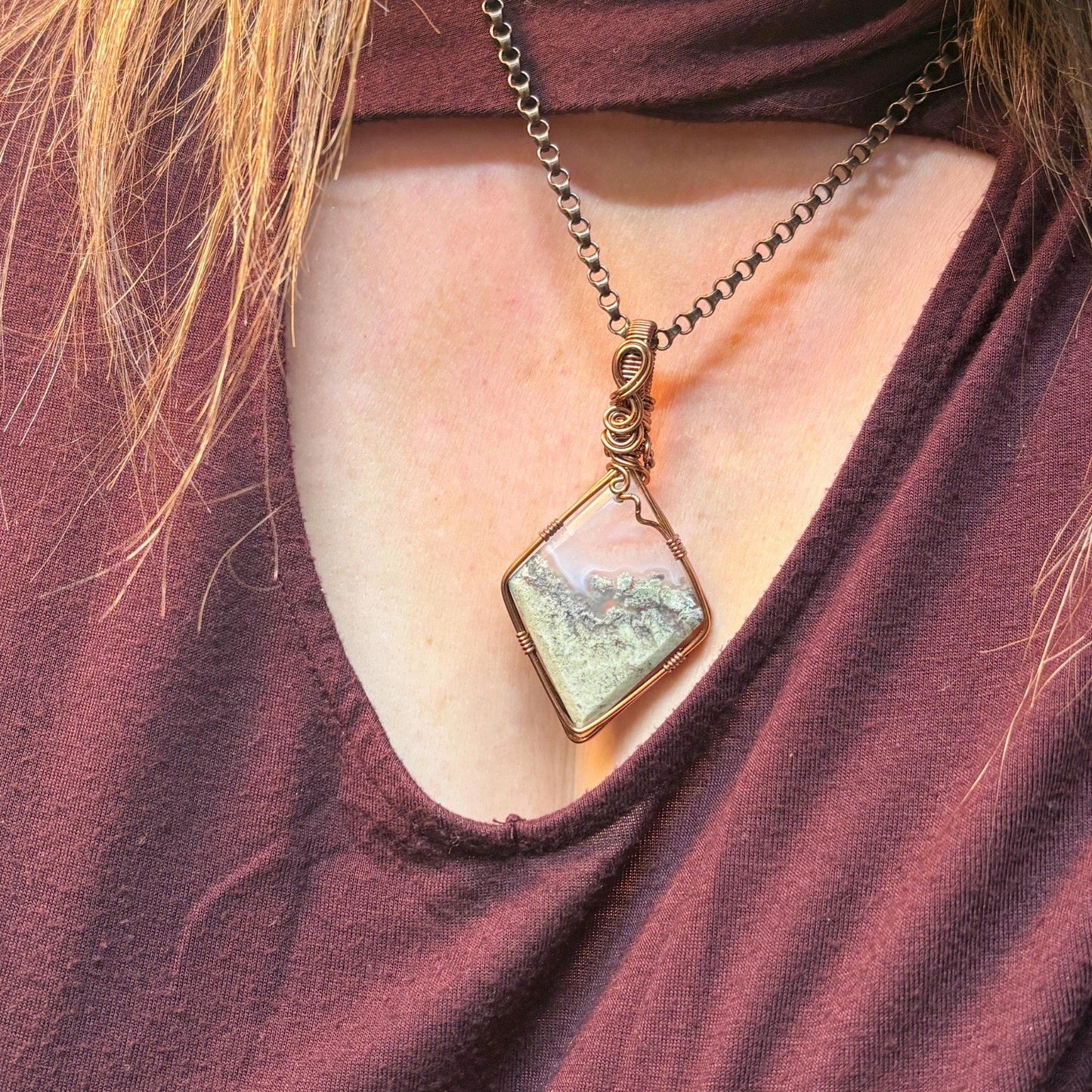 Necklace with a square pendant worn by a person in a burgundy top.