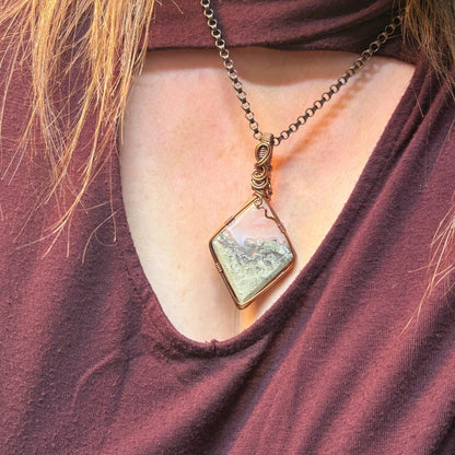 Necklace with a square pendant worn by a person in a burgundy top.