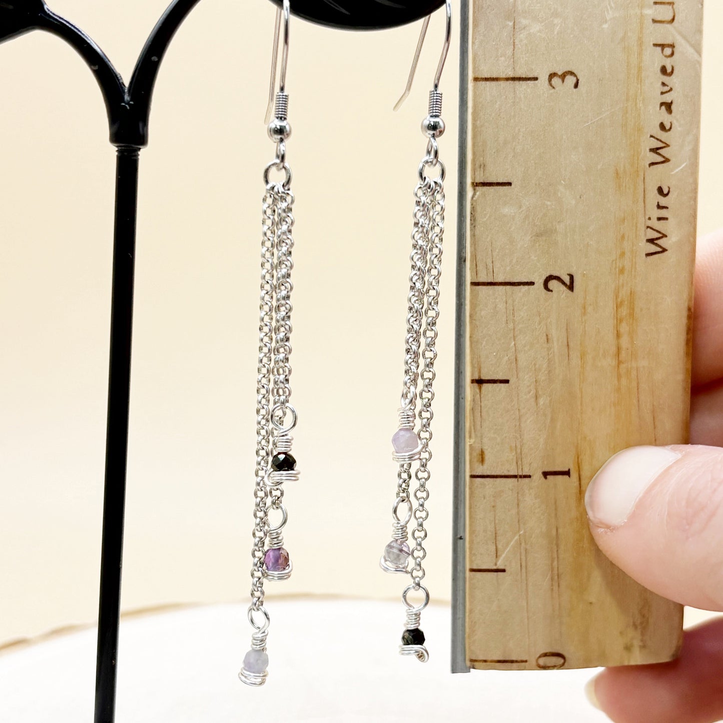 Pair of chain earrings with small beads, held against a wooden ruler for size reference.