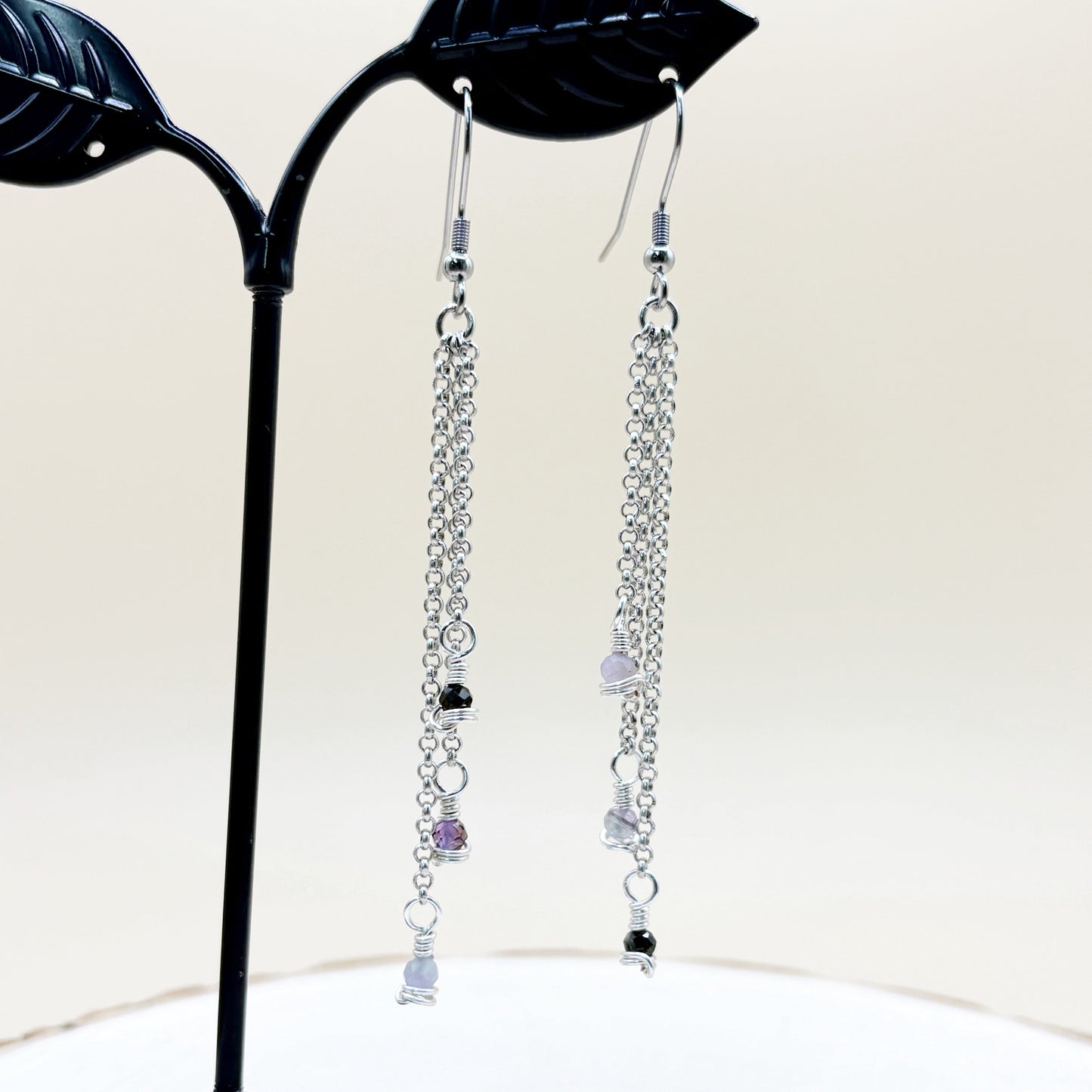 Silver chain earrings with beads on a black stand against a white background