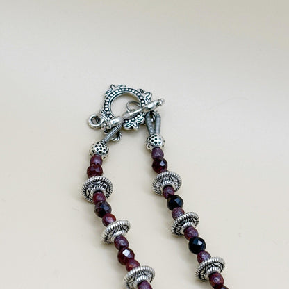 Necklace with purple beads and silver accents on a light background