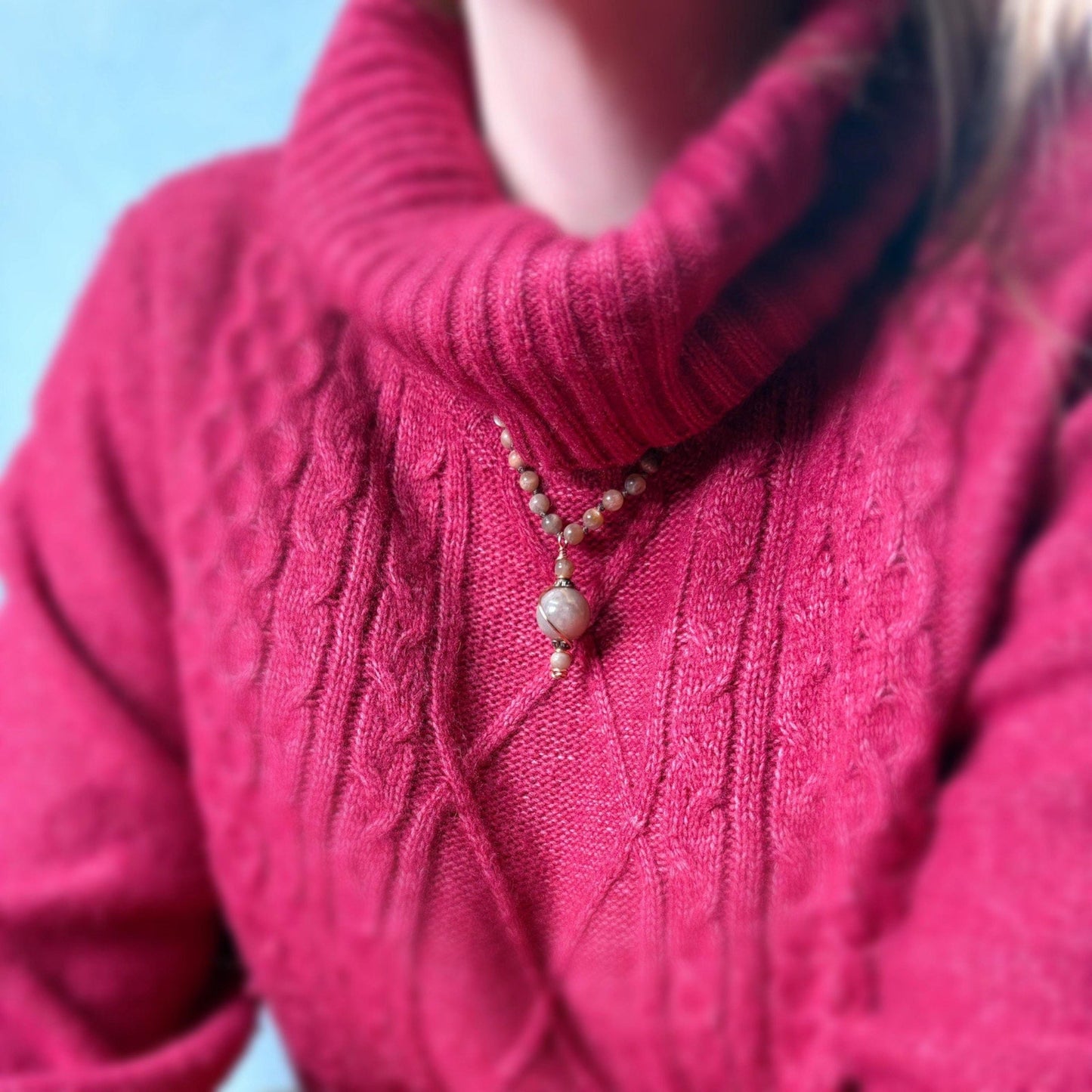 Close-up of a person wearing a pink knitted sweater with a necklace.
