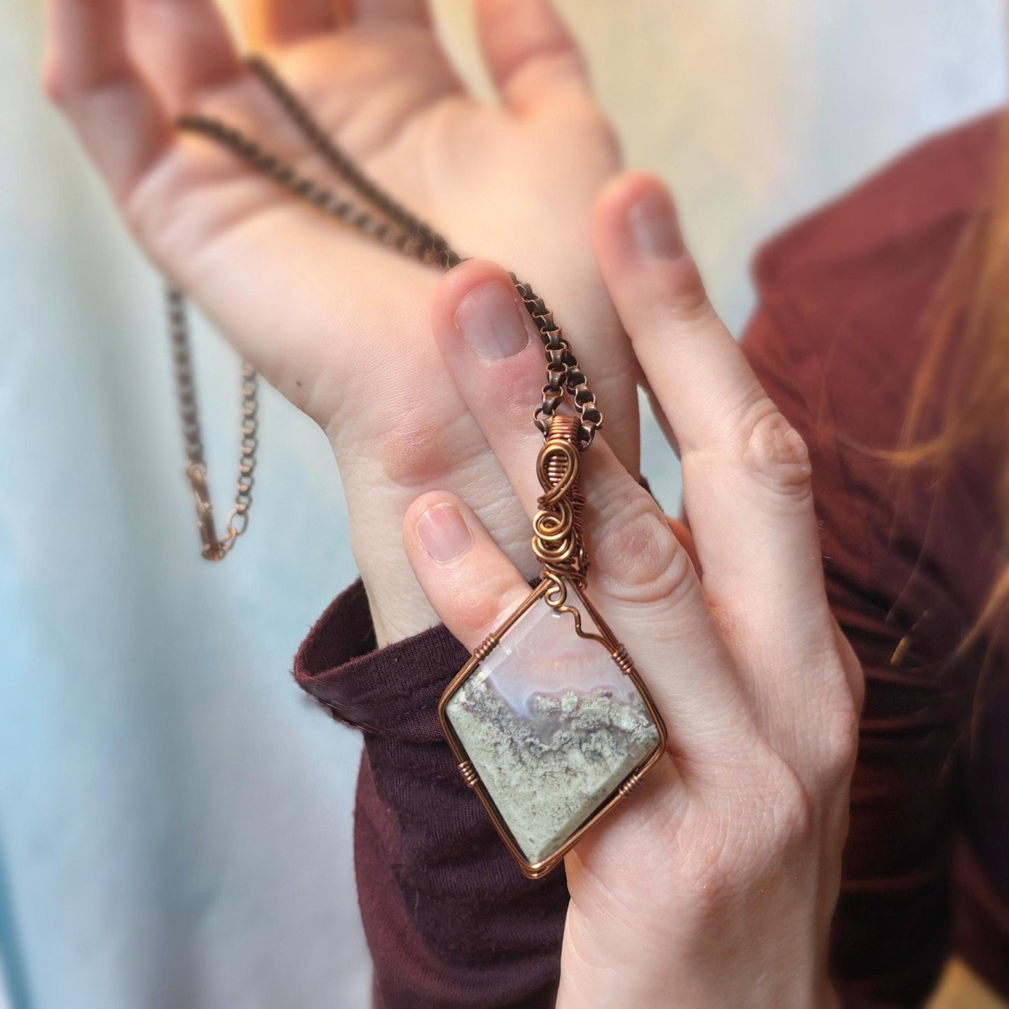 Hand holding a necklace with a textured pendant against a blurred background