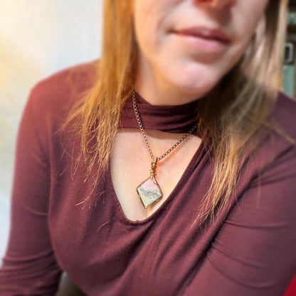 Close-up of a person wearing a maroon top with a necklace featuring a geometric pendant.