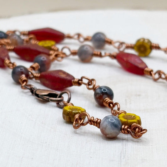 Necklace with multicolored beads and copper wire on a white wooden background