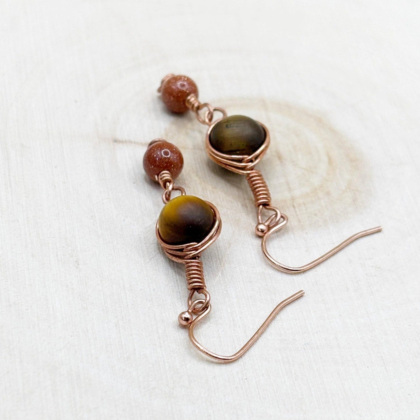 Pair of copper wire-wrapped earrings with tiger's eye stones on a white wooden background