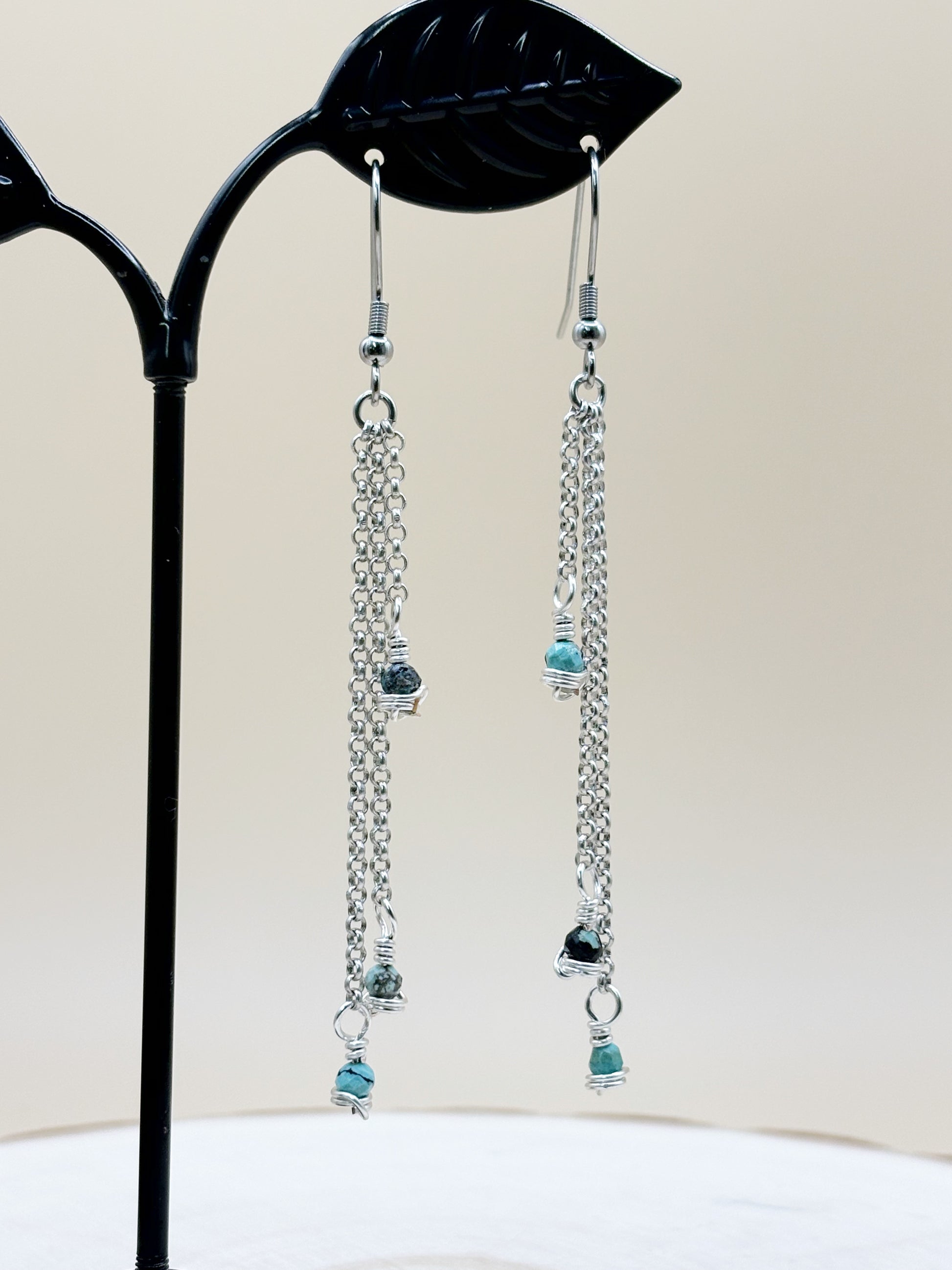 Pair of chain earrings with blue beads on a black stand.