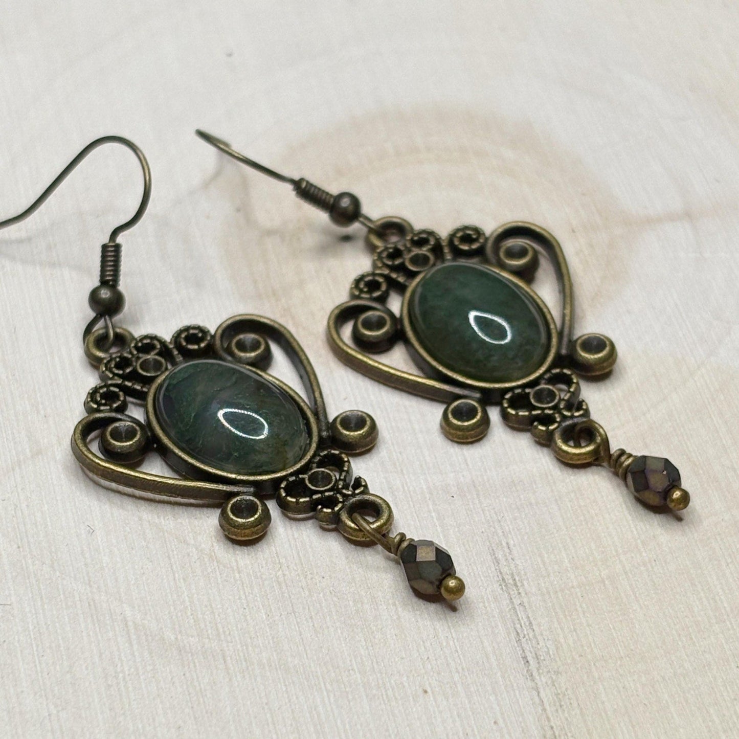 Pair of ornate earrings with dark green stones on a light background