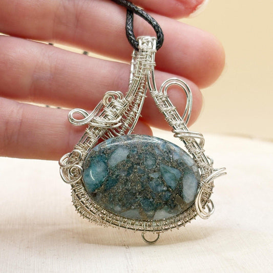 Silver wire-wrapped pendant with a blue stone held between fingers on a beige background