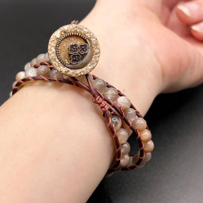 Close-up of a wrist wearing a beaded bracelet with a decorative button on a dark background