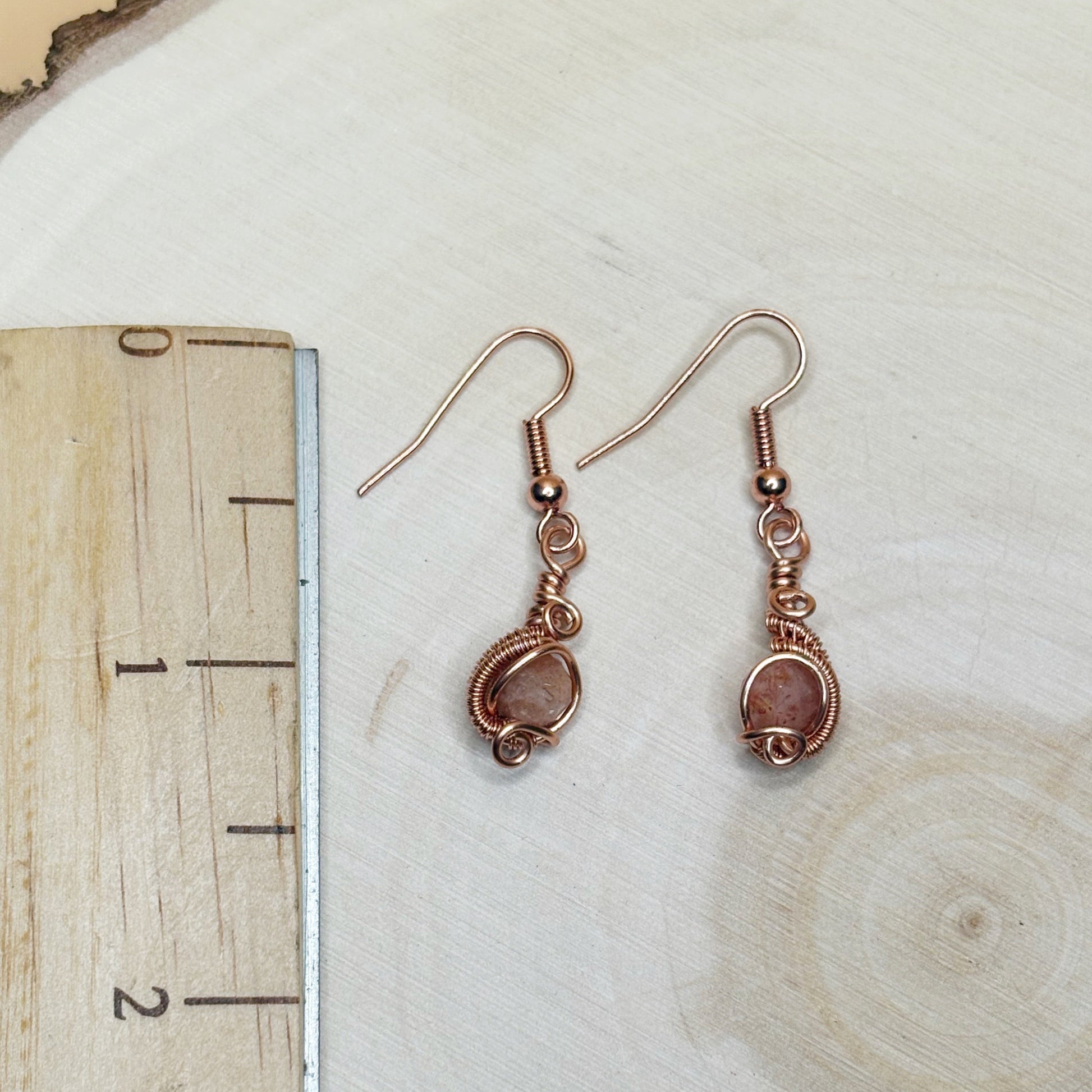 Pair of copper wire-wrapped earrings on a wooden surface with a ruler for scale.