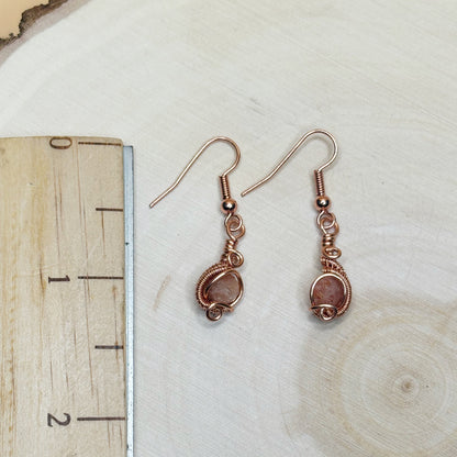 Pair of copper wire-wrapped earrings on a wooden surface with a ruler for scale.