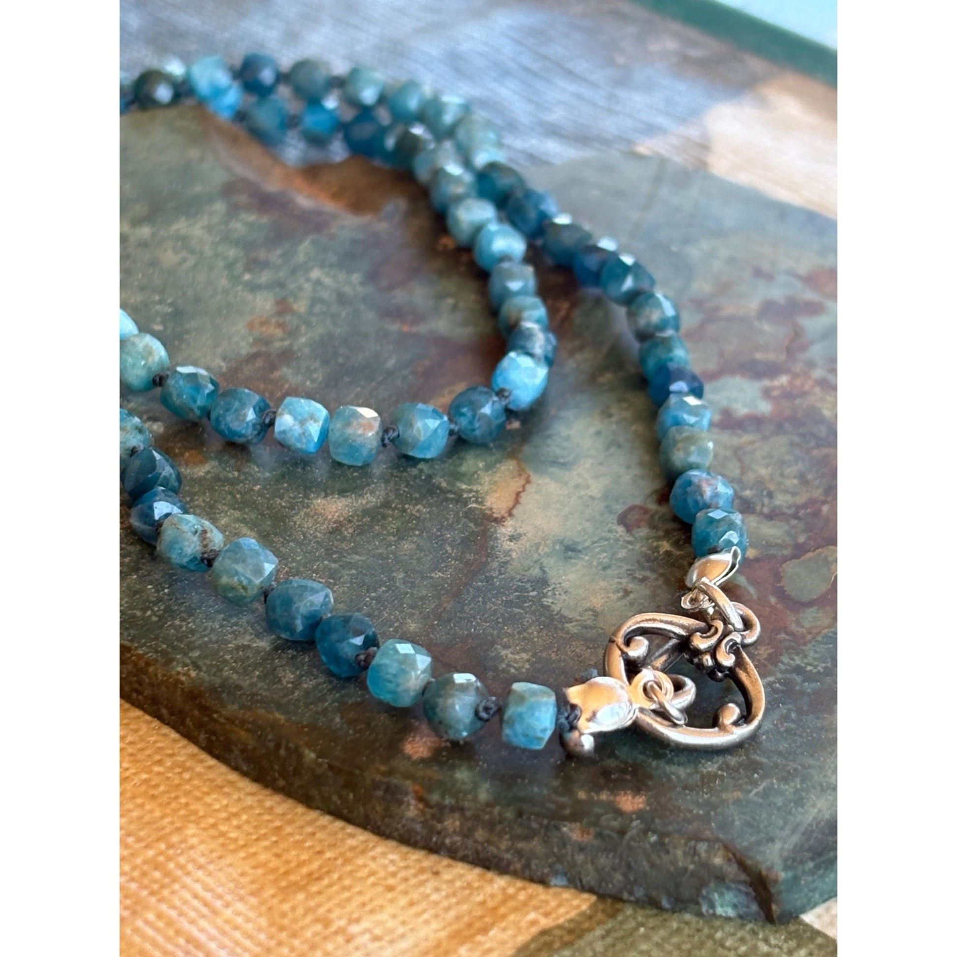 Blue beaded necklace with a silver heart charm on a textured surface