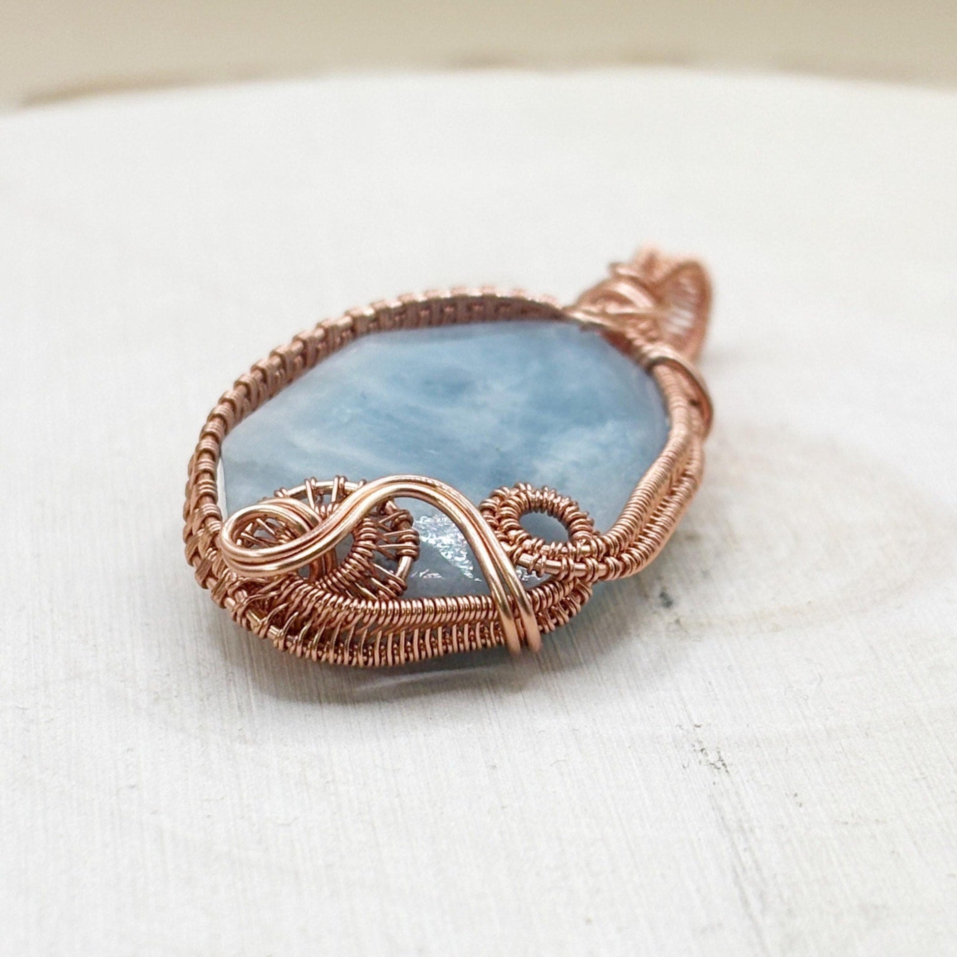 Pendant with blue stone and copper wire wrapping on a white surface