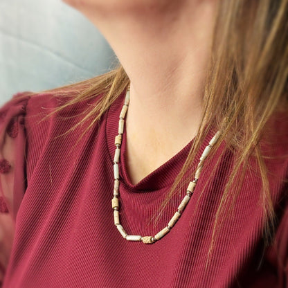 Person wearing a red top with a necklace featuring beige beads.