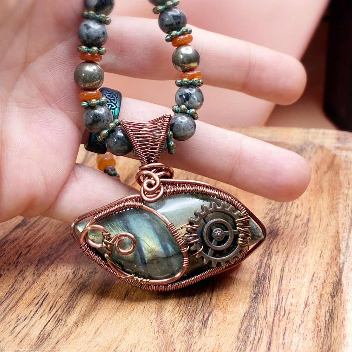 Hand holding a necklace showing size reference of the copper pendant that is hand woven in wire