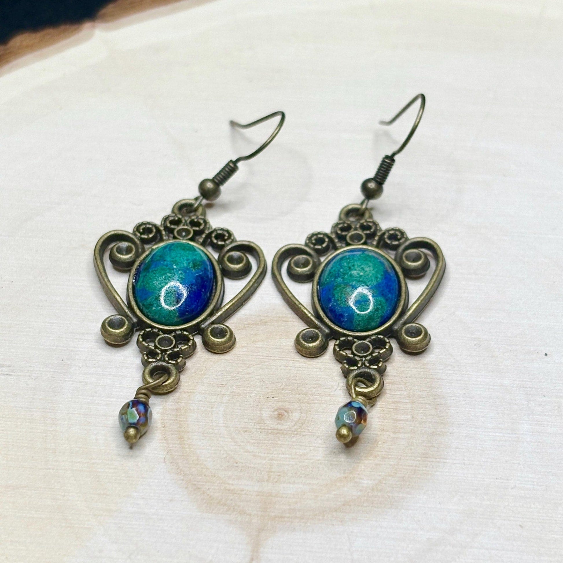 Pair of ornate earrings with blue and green gemstones on a white background