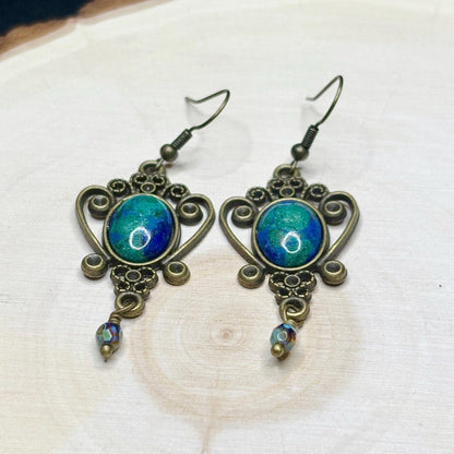 Pair of ornate earrings with blue and green gemstones on a white background
