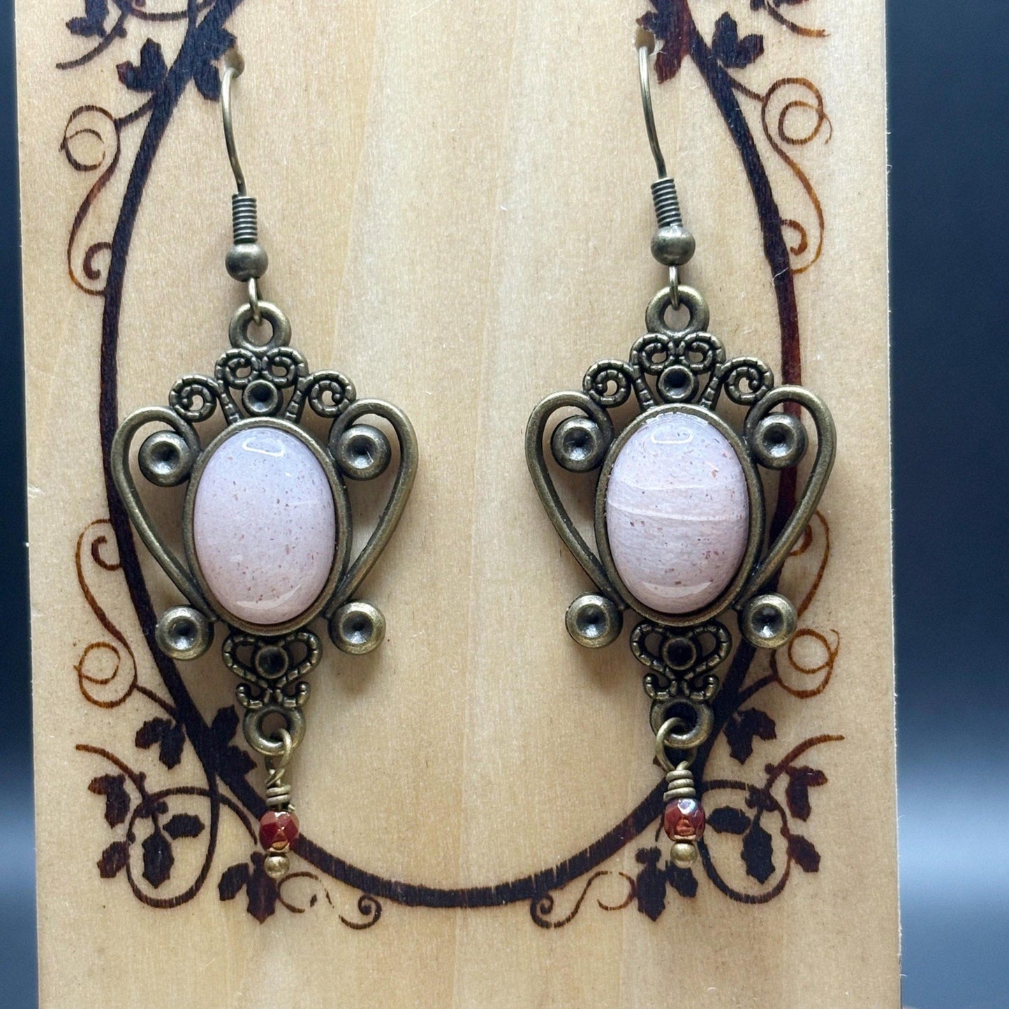 Pair of ornate earrings with pink stones on a decorative card