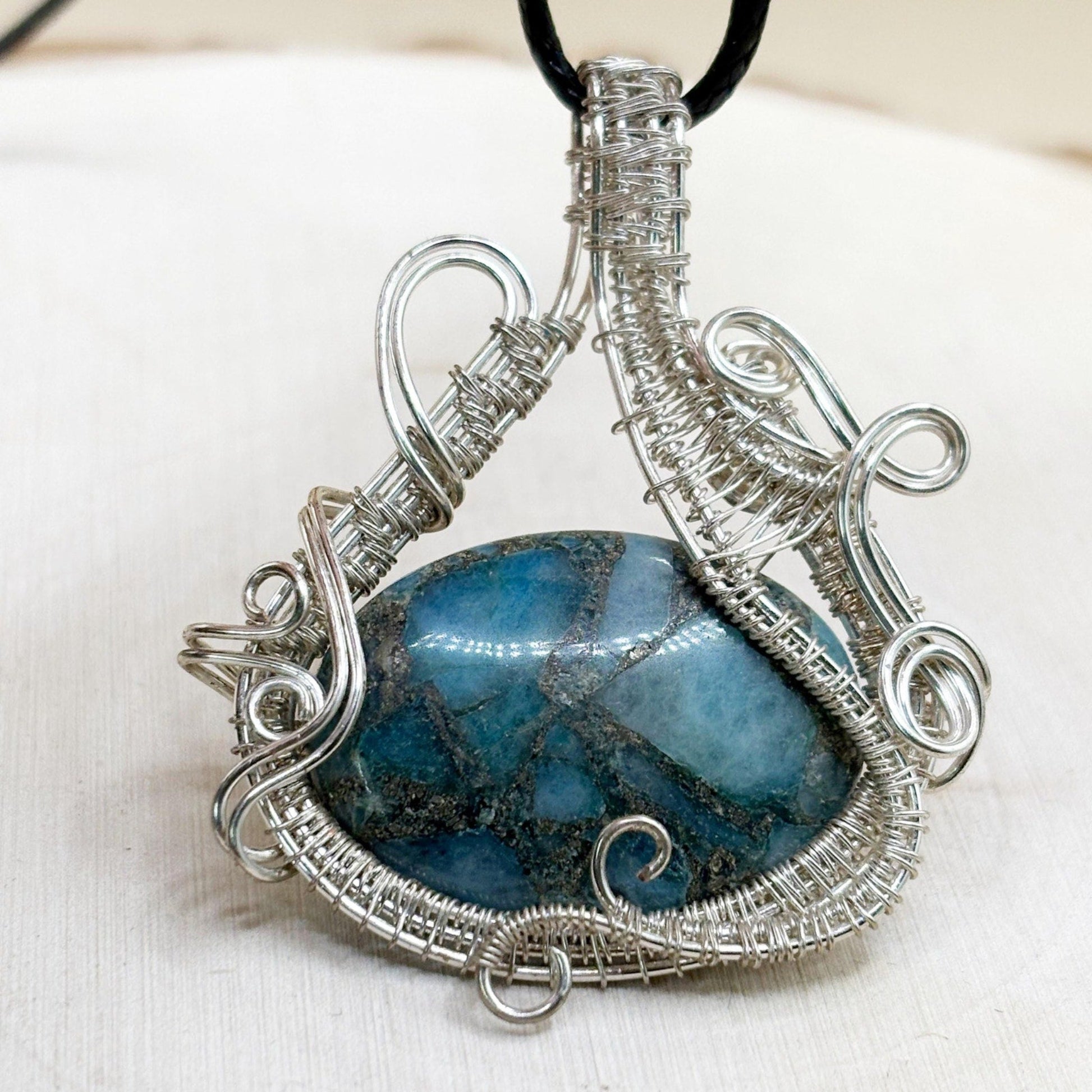Silver-wrapped pendant with a blue stone on a white background