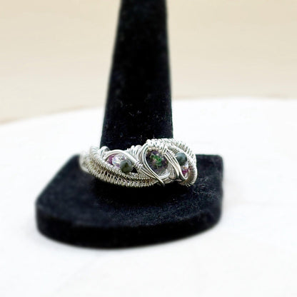 Silver wire-wrapped ring with gemstones on a black stand against a white background