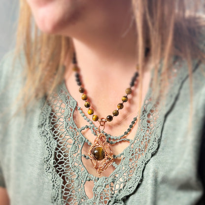 Necklace with tiger's eye stones on a person wearing a lacey green top.