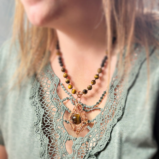 Necklace with tiger's eye stones on a person wearing a lacey green top.