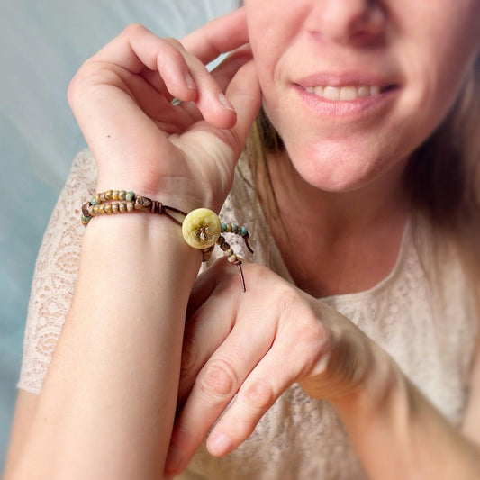 Close-up of a woman wearing a bracelet with a yellow bead on a neutral background
