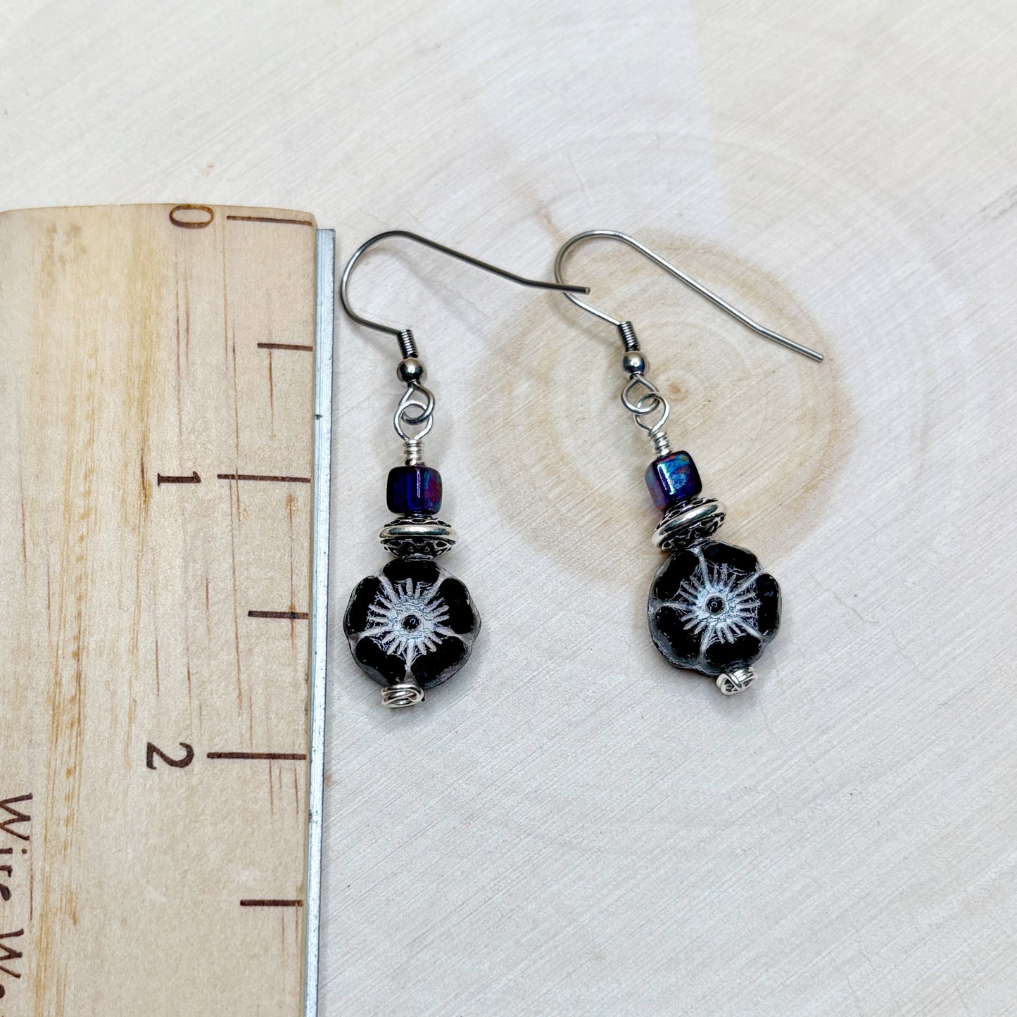 Pair of black beaded earrings with silver hooks on a white background with a heart-shaped object.