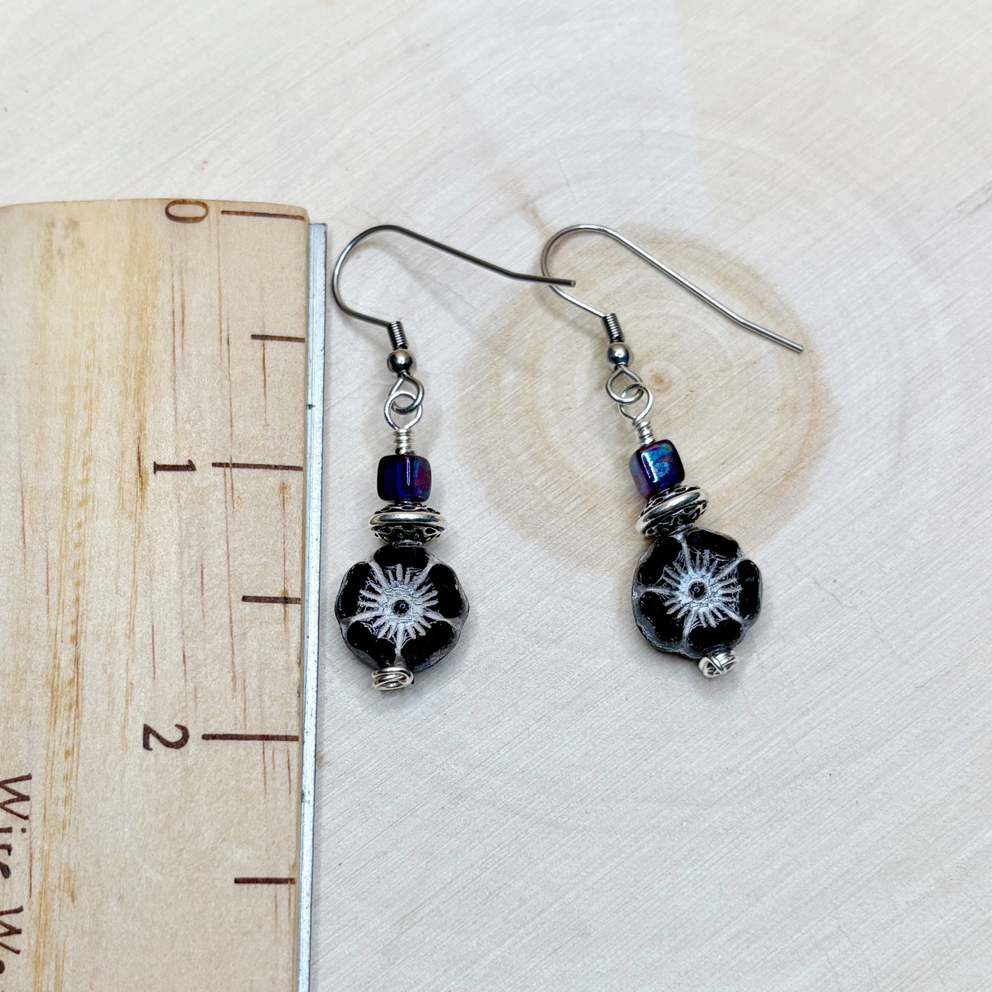 Pair of black beaded earrings with silver hooks on a white background with a heart-shaped object.