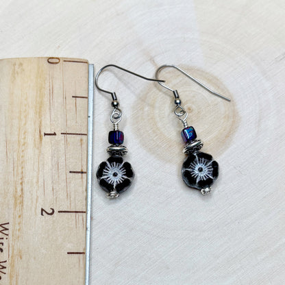 Pair of black beaded earrings with silver hooks on a white background with a heart-shaped object.