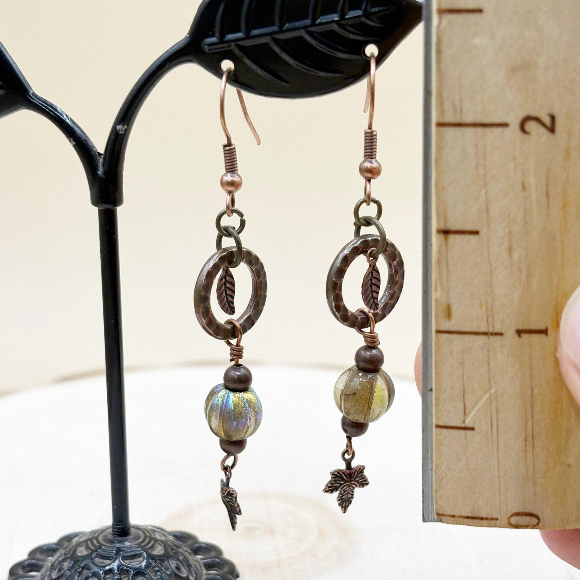 Pair of earrings with iridescent czech glass beads and leaf designs on a stand.