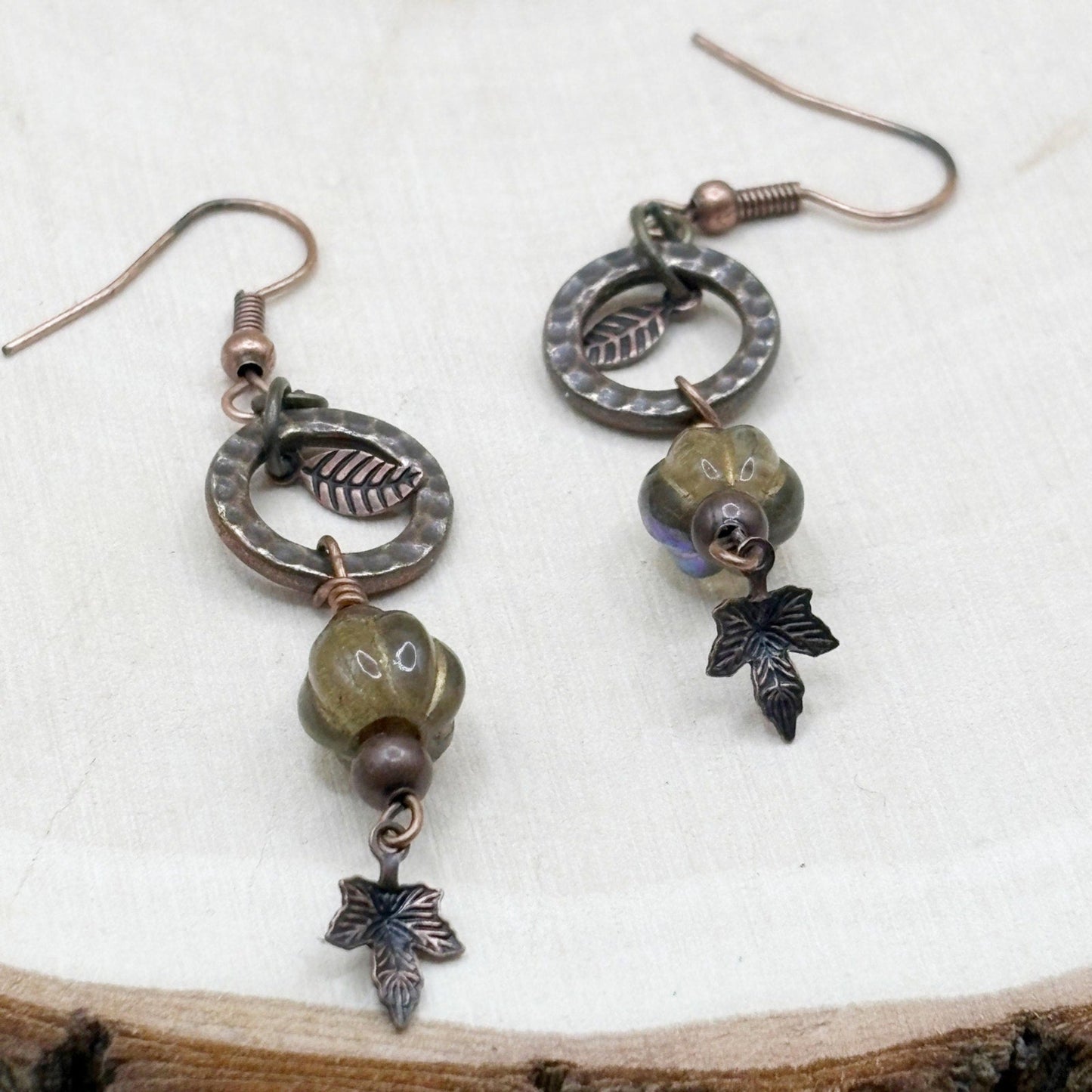 Pair of earrings with maple leaf and bead designs on a wooden surface