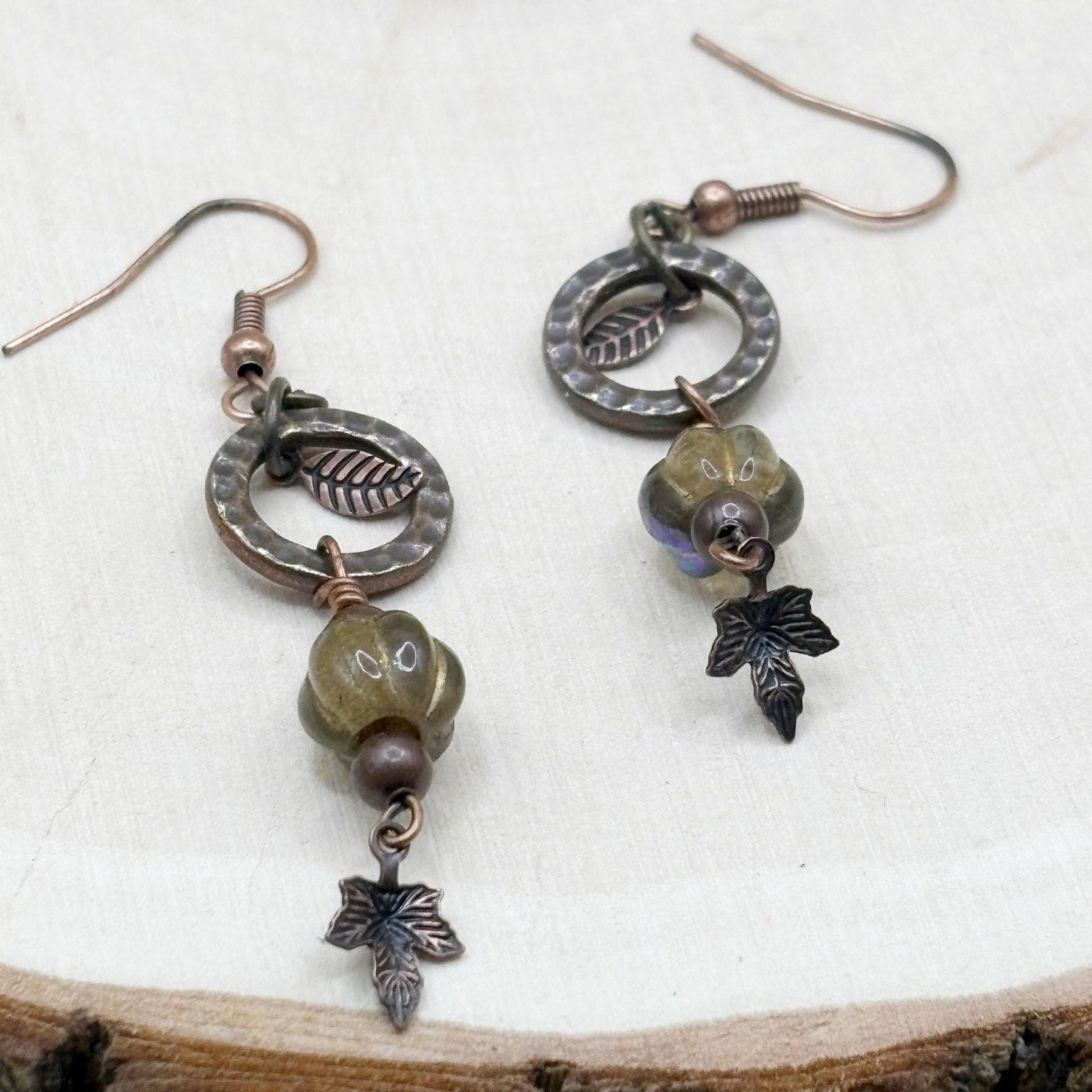 Pair of earrings with maple leaf and bead designs on a wooden surface
