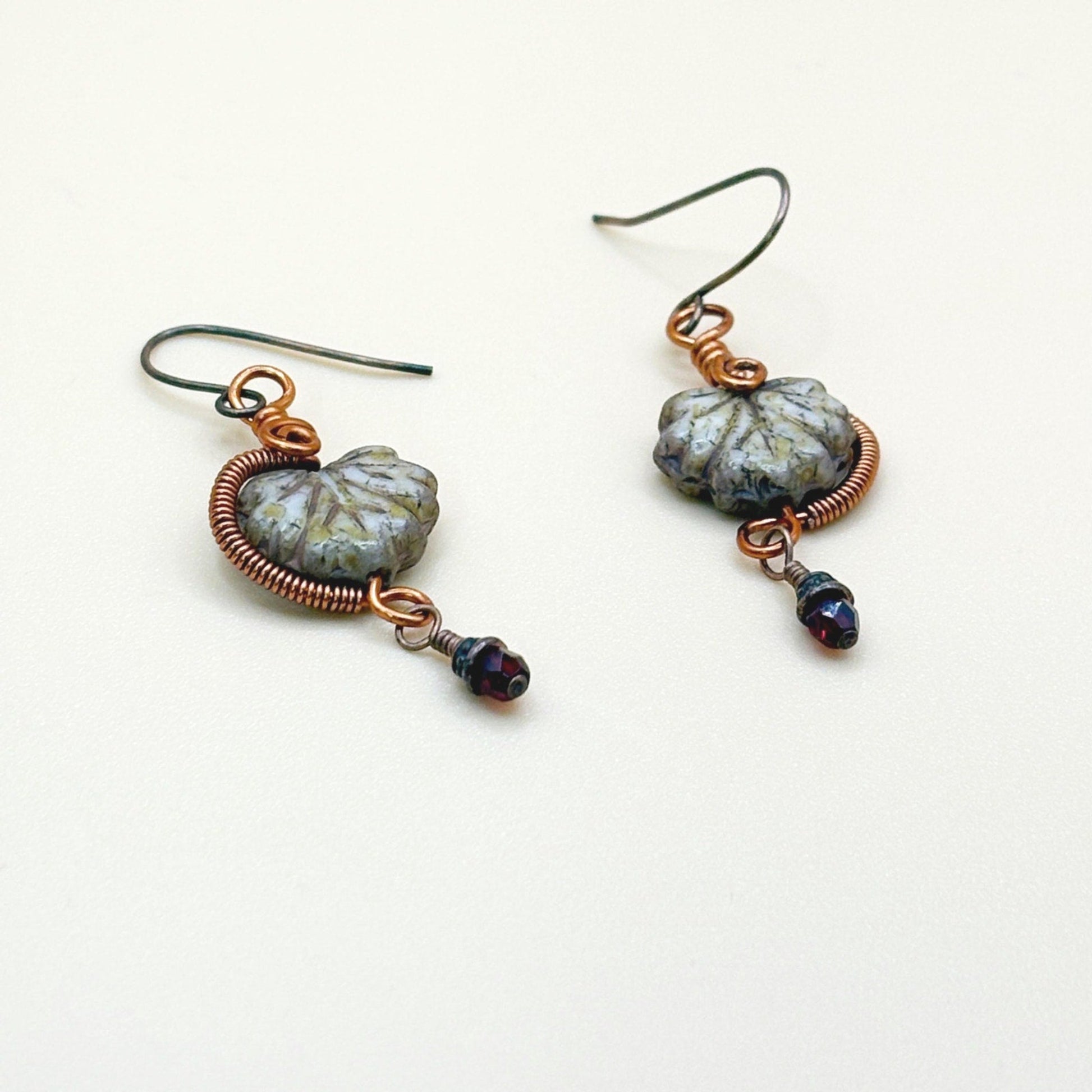 Pair of earrings with glass maple leaf beige beads and copper wire on a white background