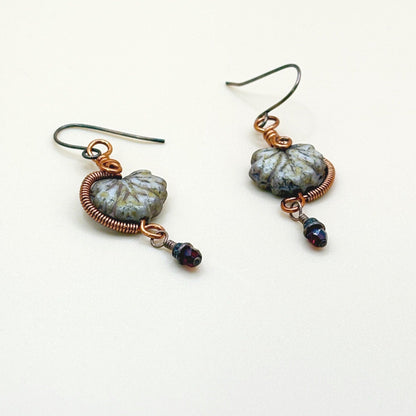 Pair of earrings with glass maple leaf beige beads and copper wire on a white background