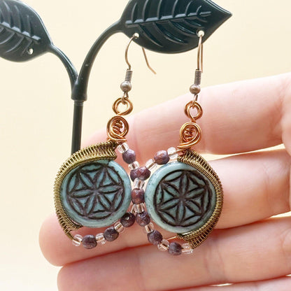 Pair of earrings with circular designs held by a hand against a neutral background