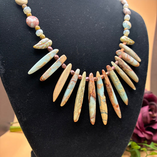 A statement necklace made of natural turquoise and brown color tones stone tooth-shaped spikes, displayed on a black velvet jewelry bust.