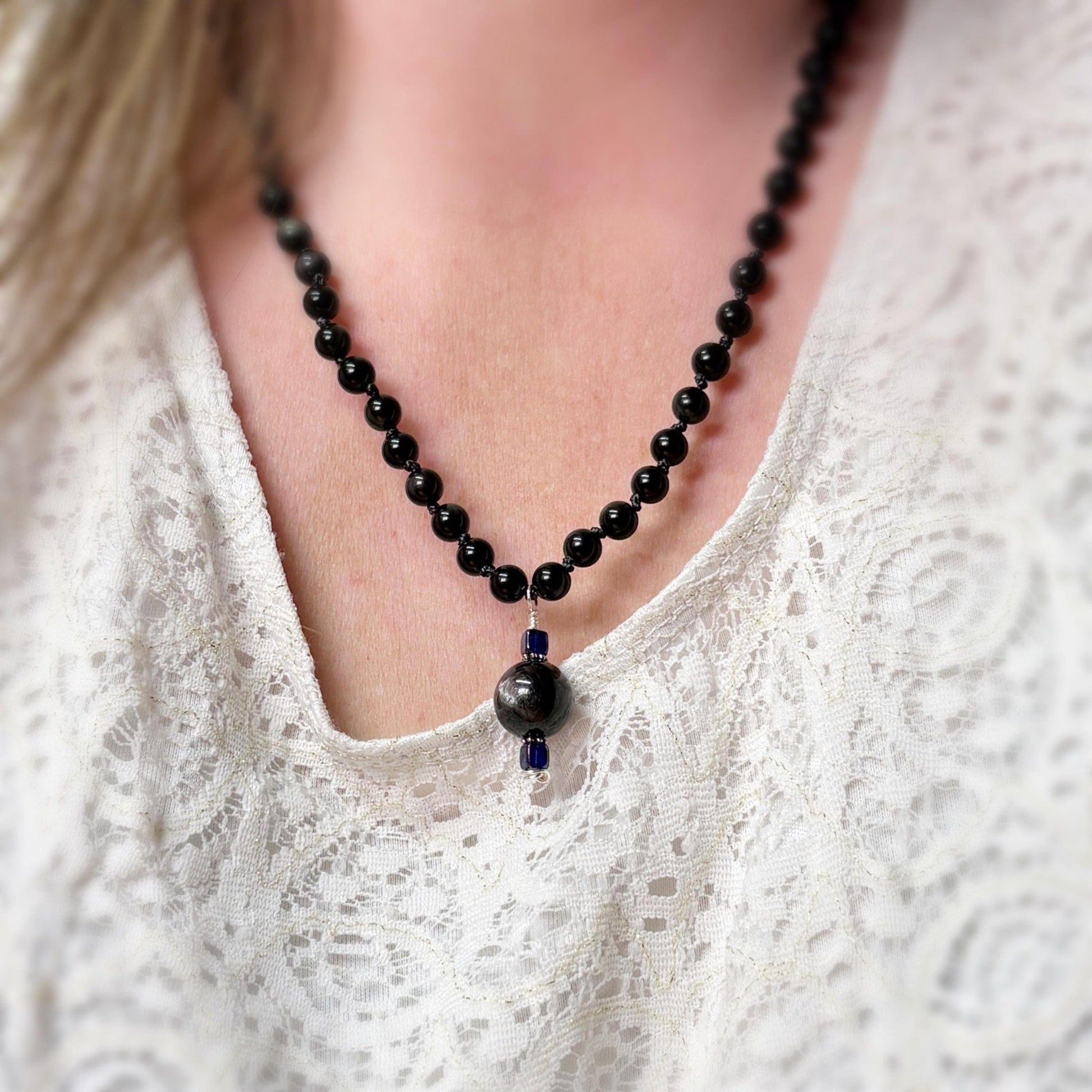 Black beaded necklace with a blue accent worn by a person in a white lace top.