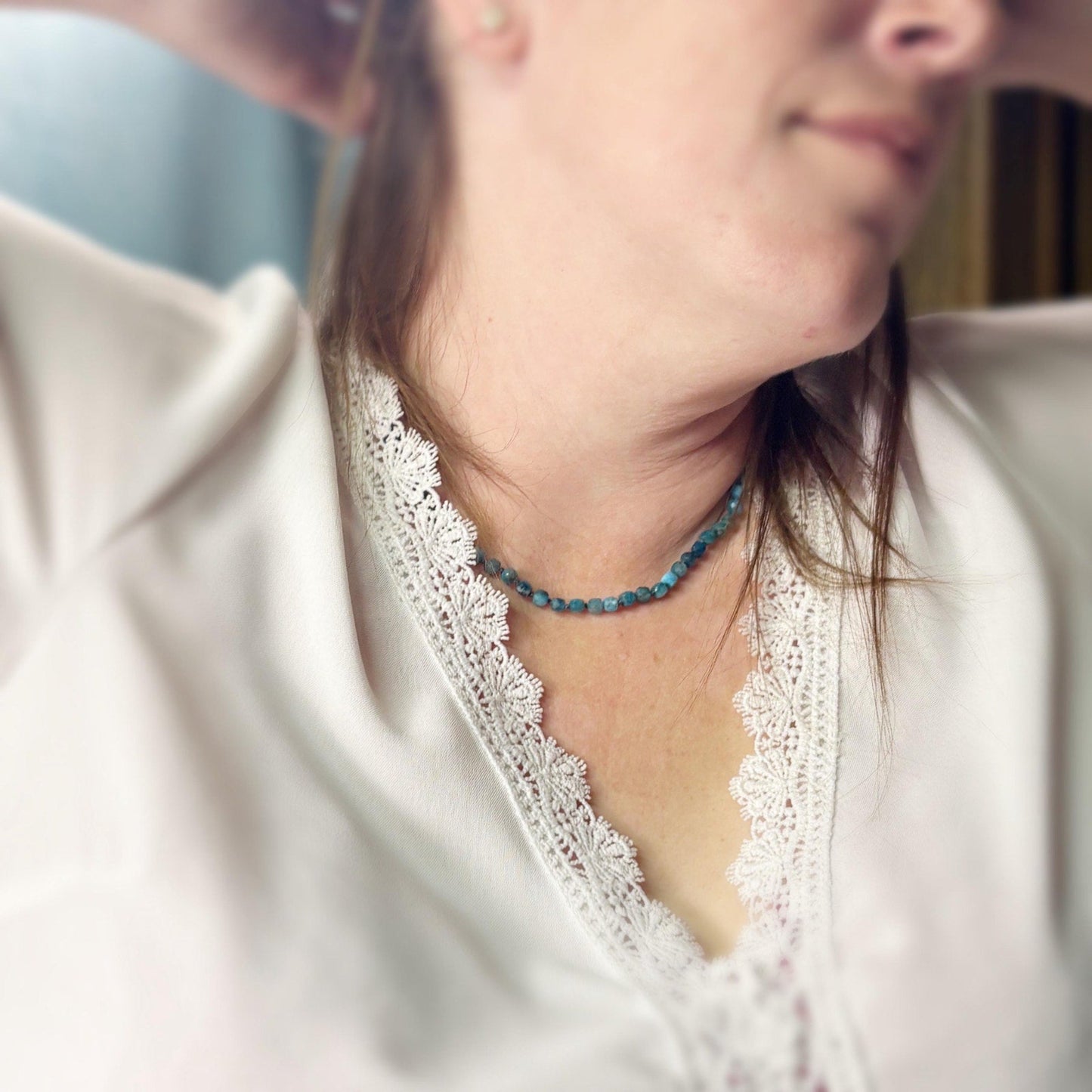 Close-up of a person wearing a white lace top and a blue beaded necklace.