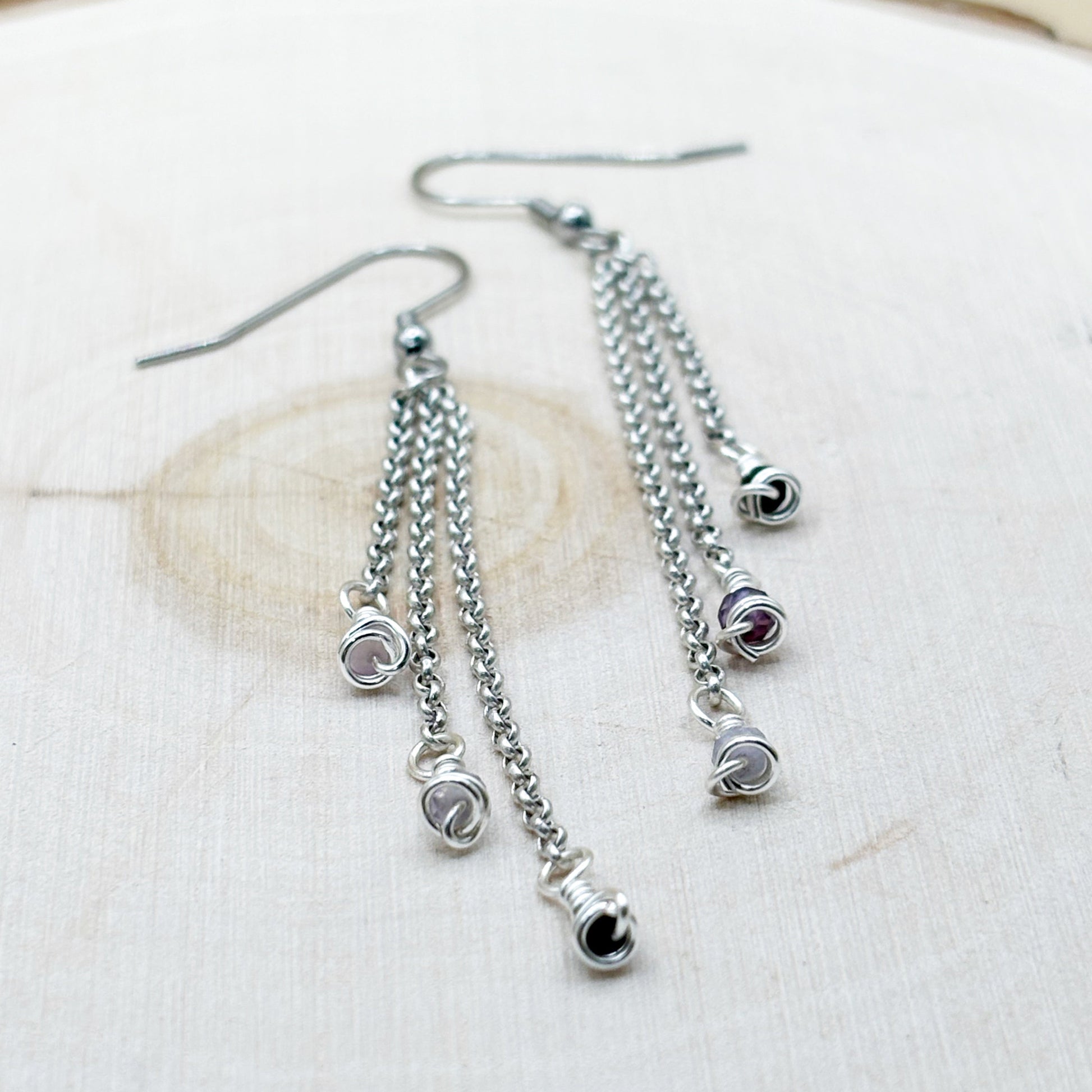 Silver chain earrings with small round charms on a white fabric background