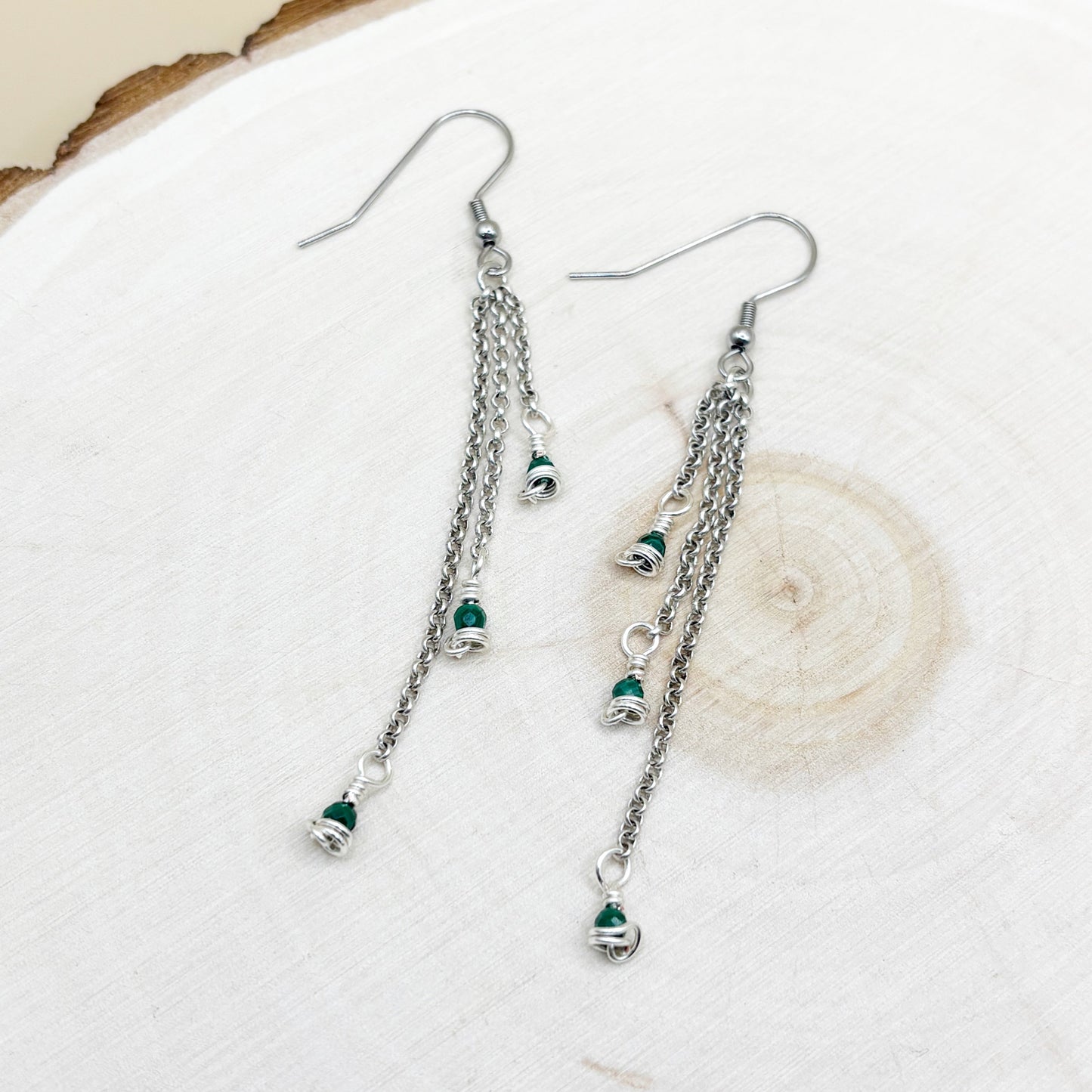 Silver chain earrings with green beads on a white background
