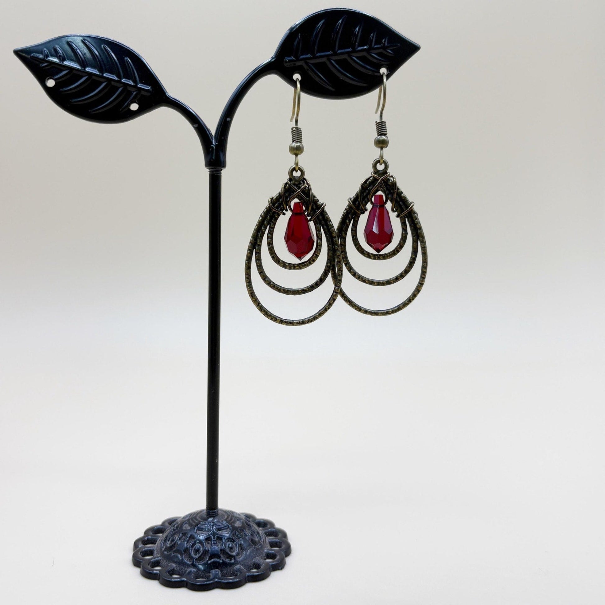 Pair of earrings with red teardrop stones on a black leaf-shaped stand against a white background