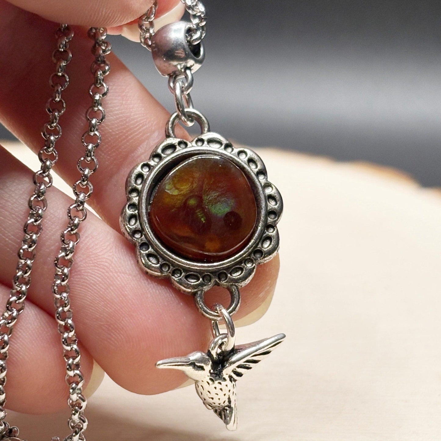 Close-up of a silver pendant with a brown stone and bird charm held by a hand.