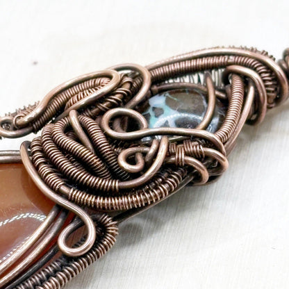 Copper wire pendant with a central gemstone on a white background