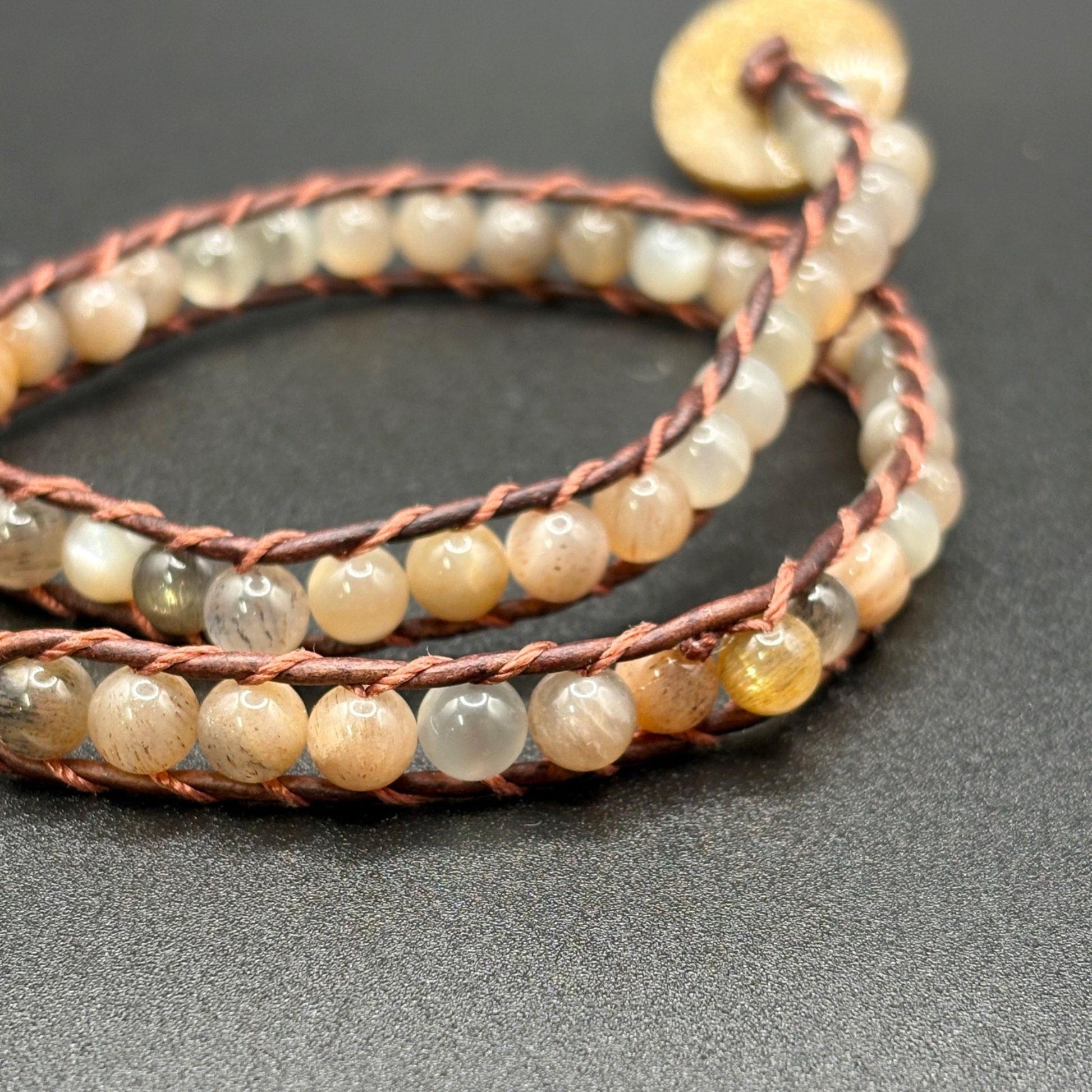 Multistrand beaded bracelet with brown leather cord on a dark surface