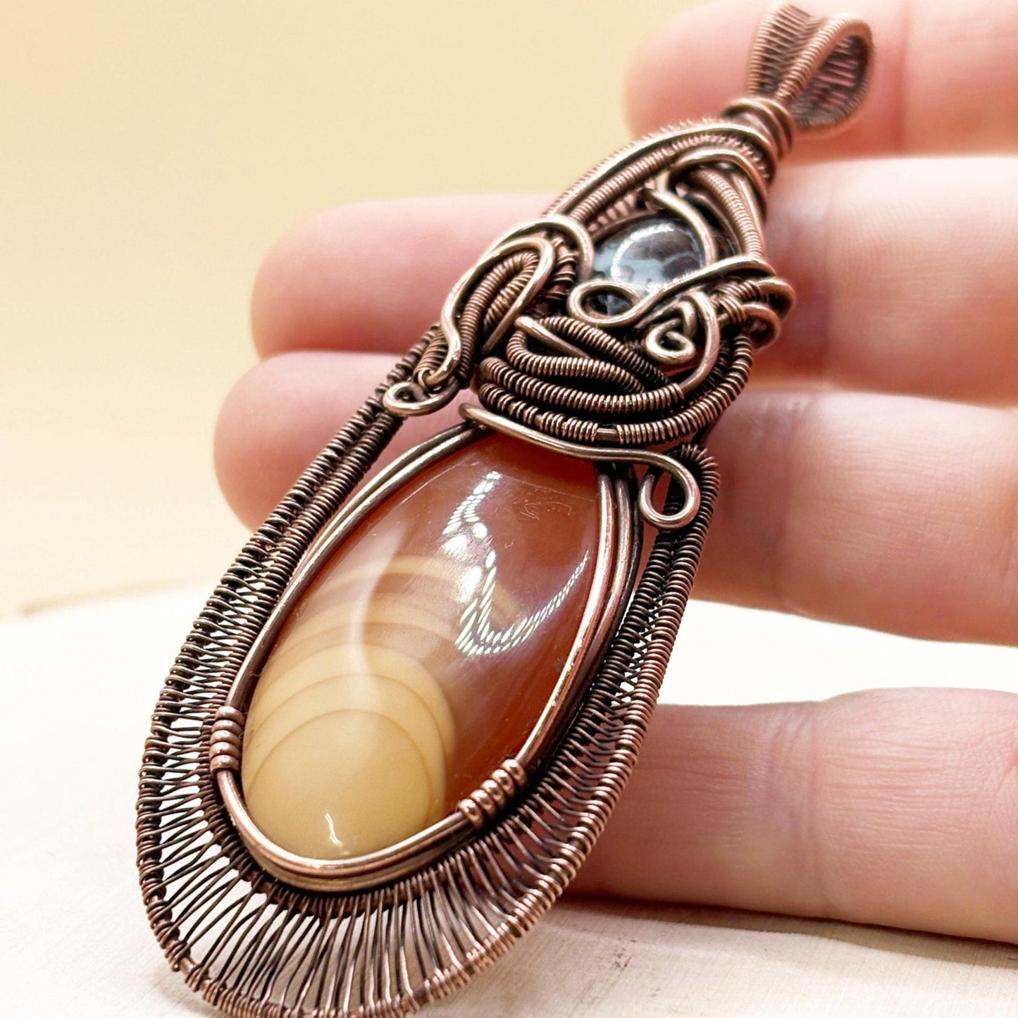 Copper-wrapped pendant with a central stone held between fingers against a neutral background