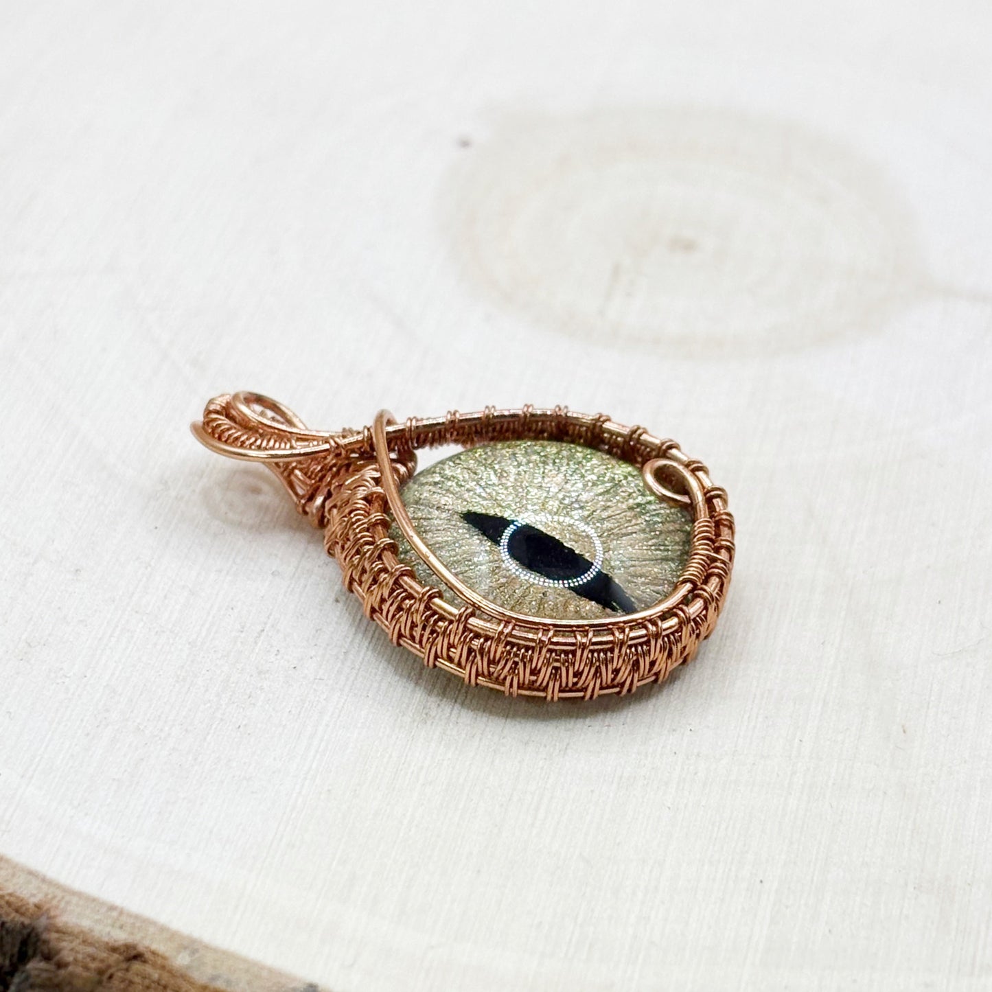 Decorative pendant with eye design in a copper wire frame on a white wood background