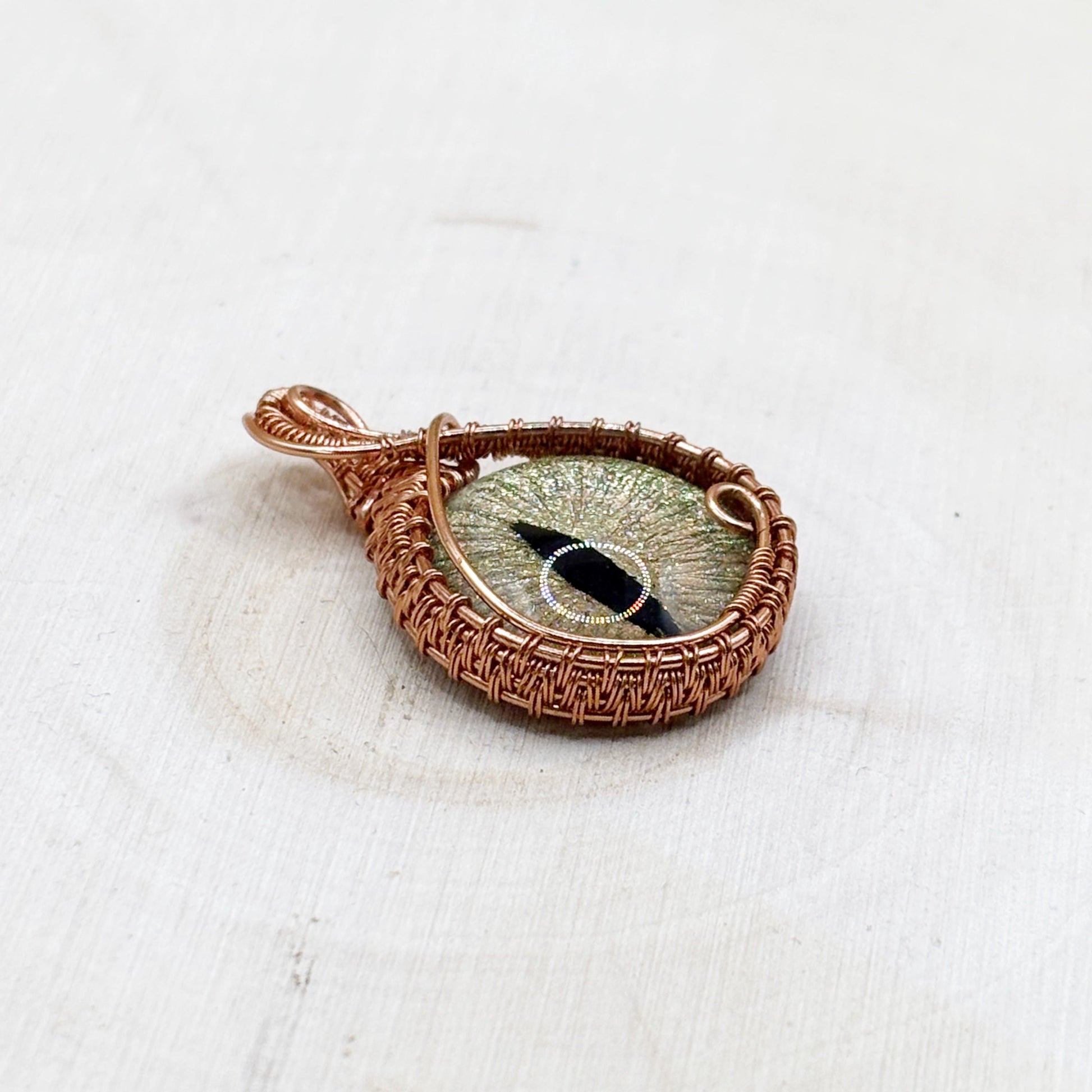 Copper-wrapped pendant with a central painted glass eye on a white fabric background