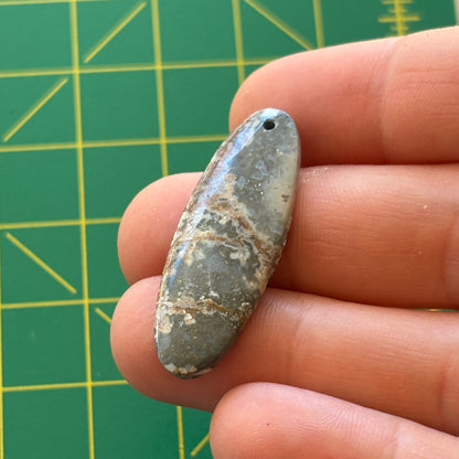 Oval-shaped stone held between fingers against a green grid background